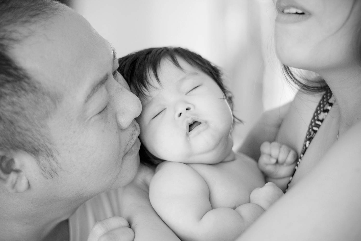 loving parents enjoying baby time with little girl in between them at photographer studio in olive branch ms black and white backdrop lighting asian family by danielle jacqueline