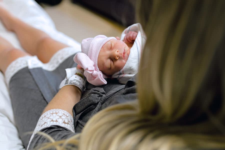 photograph peeking over mommy's should while on hospital bed in gown at newborn baby girl captured by danielle jacqueline for pregnant packages for expecting parents portraits in desoto county ms