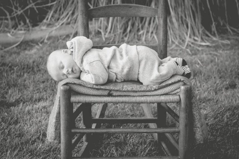 little boy in onesie laying on wicker rocking chair outside during professional portrait session by danielle jacqueline photography baby ideas in memphis tn grass and quilt black and white