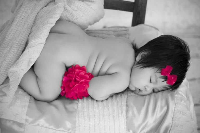 little newborn girl laying on quilt atop chair facing side asleep with black and white edit but pink flower and bow highlighted to give baby picture ideas extra effect by daniele jacqueline photography in memphis tennesse