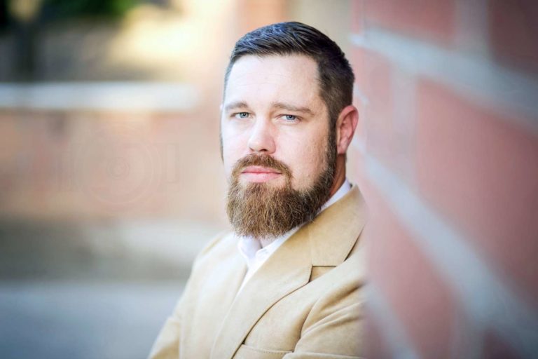 brick wall in focus looking towards president of olive branch company for headshot session outdoors by danielle jacqueline photography