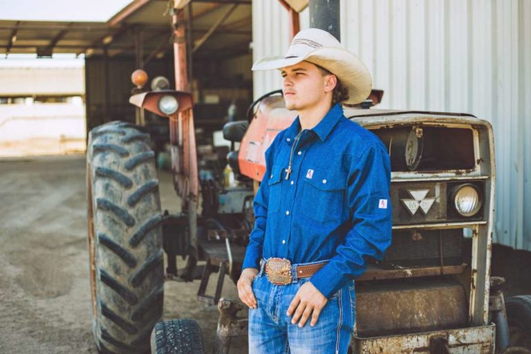 american clothing line actor and bull rider standing by tractor blue denim wrangler jeans and 4 gallon hat looking to left outdoors in desoto county mississippi by danielle jacqueline photography