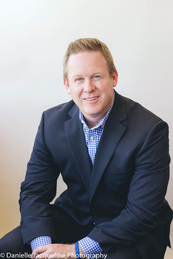 business man leaning on knees sitting on stool at photography studio in olive branch mississippi for professional headshots with danielle in formal suit and slacks