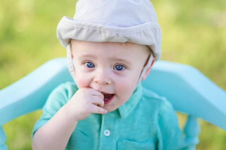 hand in mouth 11 mo old infant boy turquoise shirt and baby blue wooden chair seated in middle of grass field at desoto county park by danielle jacqueline photography