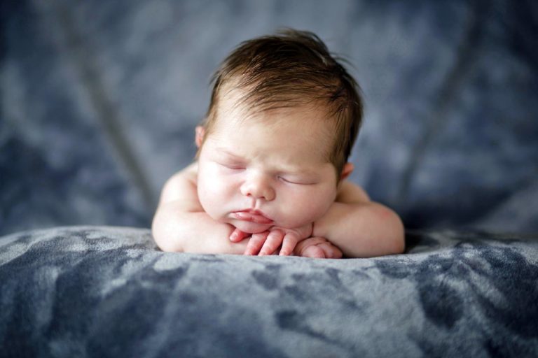 hands folded under chin scrunched face eyes closed baby picture ideas in studio soft dark microfiber blanket over pillow good lighting by memphis photographer danielle jacqueline