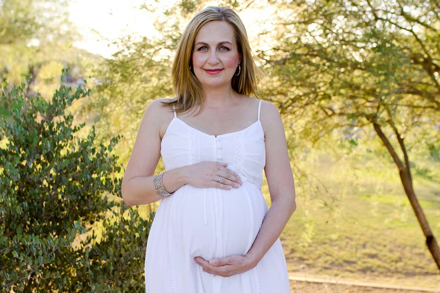 mommy to be cupping pregnant belly with hands in white sun dress outdoors for maternity photography session with danielle jacqueline in olive branch ms