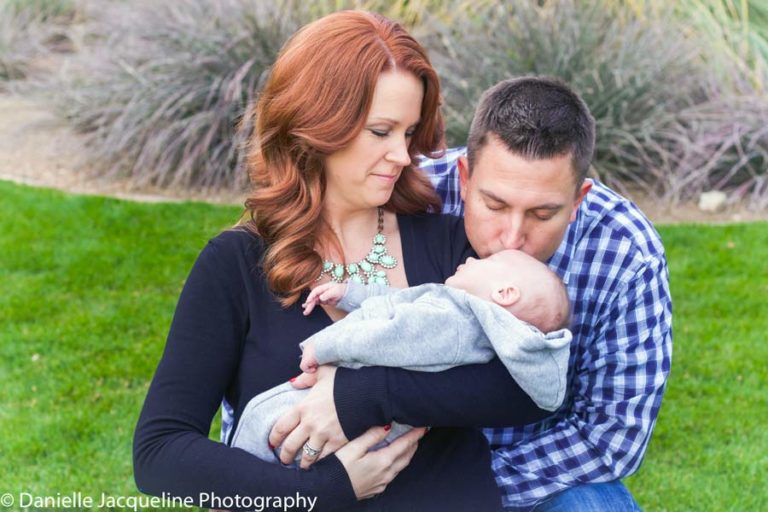 daddy kissing newborn daughter on the forehead while she's in mother's arms outside their home sitting in grass pregnancy expecting photos by danielle jacqueline memphis families