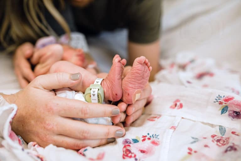 mothers hand painted fingernails holding feet of baby girl just born flowered blanket on hospital bed during fresh 48 session by danielle jacqueline photography