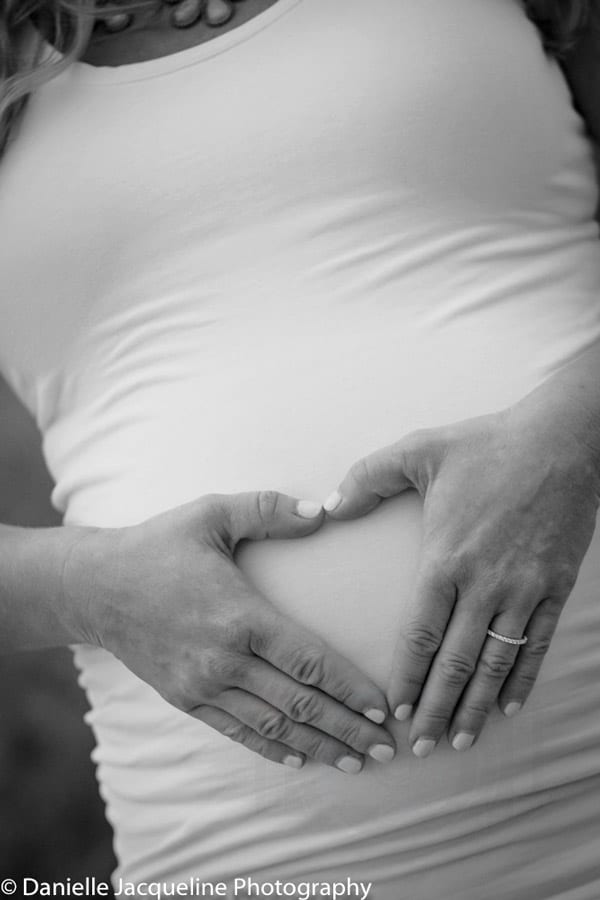 angled black and white photo of expecting mother's hands over pregnant belly in the shape of a heart of danielle jacqueline photography's maternal portraits page for desoto county and memphis services