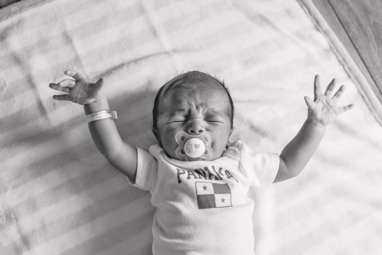 black and white newborn boy on striped hospital blanket arms raised up binky in mouth crying crinkled forehead portrait by danielle jacqueline photography