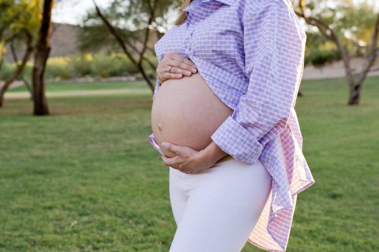 beautiful baby bump woman in husband's purple dress shirt and white tights grass field with distressed trees in mississippi background by danielle jacqueline photography desoto county