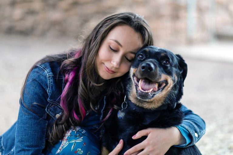 purple and pink highlights in hair jean jacket and blue dress with flowers eyes closed holding pet dog on steps outside for photography session with danielle jacqueline