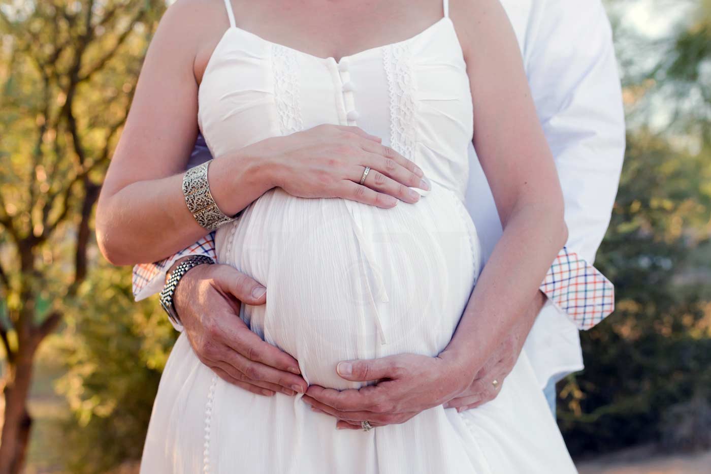 beautiful white dress pressed down on pregnant belly of mother to be in outdoor memphis tn setting for maternity session by danielle jacqueline photography with husband