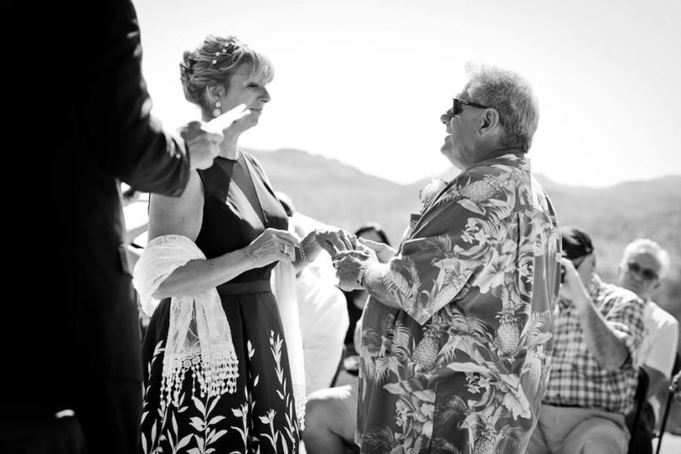 groom in Hawaiian shirt holding his bride to be's hands as he looks into her eyes and makes his vows to her with preacher in view and those in attendance with desoto county wedding photographer danielle jacqueline out of mississippi