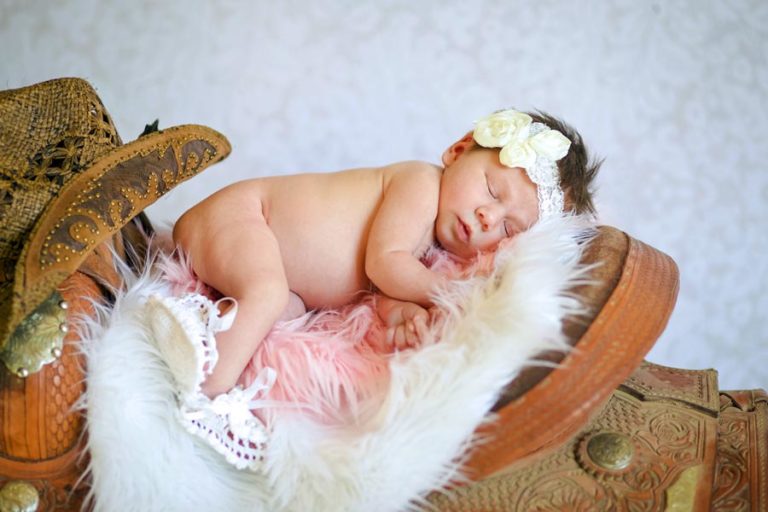 professional studio newborn portraits in desoto county ms by danielle jacqueline photography in studio with saddle set up and cowboy hat furry blanket and white flowered backdrop for proud mom