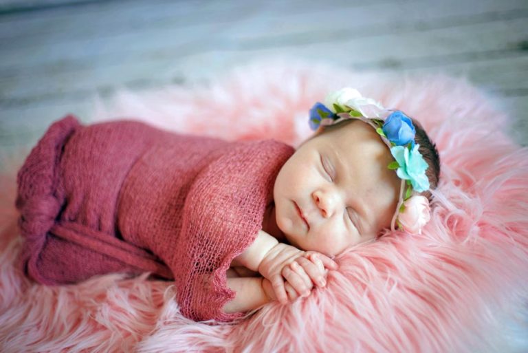 folded hands small smile newborn infant girl photography on pink plush blanket and maroon shawl wool flower headdress wood panels studio portraits danielle jacqueline in olive branch ms