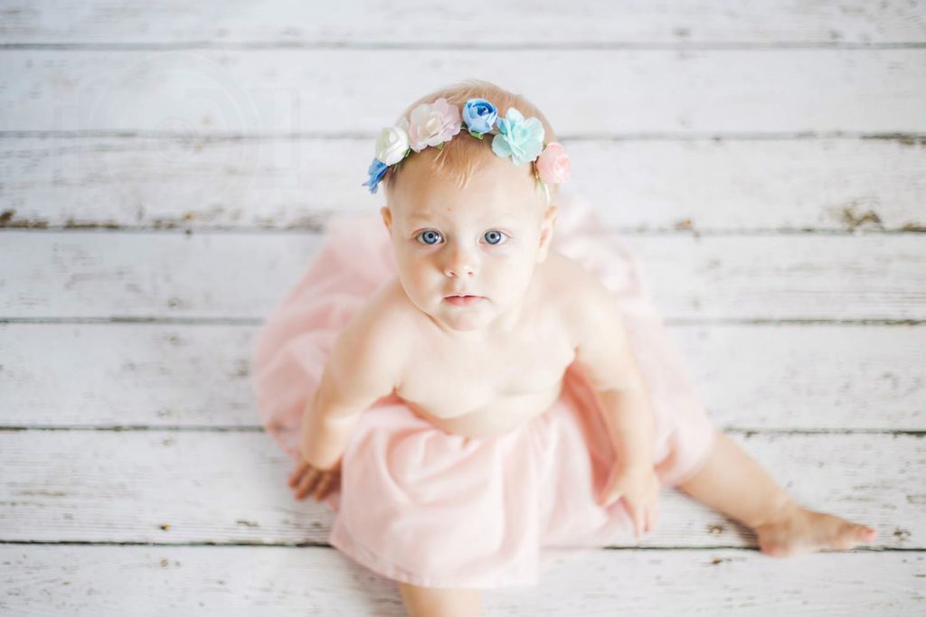 cora princess in tutu pink wood floor looking up at camera during infant photography for happy mississippi parents of 9 month old girl memphis