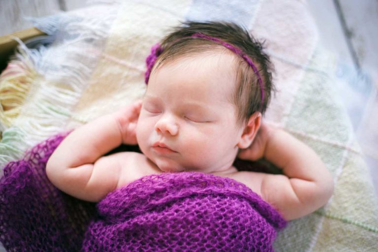 hands behind head lounging baby positioned by photographer danielle jacqueline during newborn studio portraits in desoto county ms quilt purple throw over headband for girls