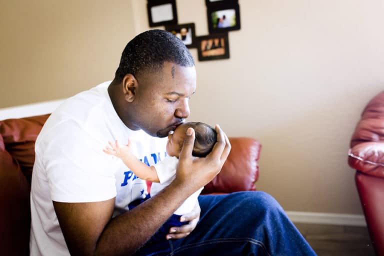 poppa bear holding his newborn infant son tightly after bringing him home for the first time sitting on couch matching family outfits olive branch ms photographer danielle jacqueline