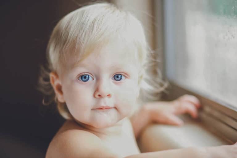 big blue eyed infant girl 11 months old holding window ledge turning head to left to look at danielle jacqueline photographer curls cutie olive branch ms