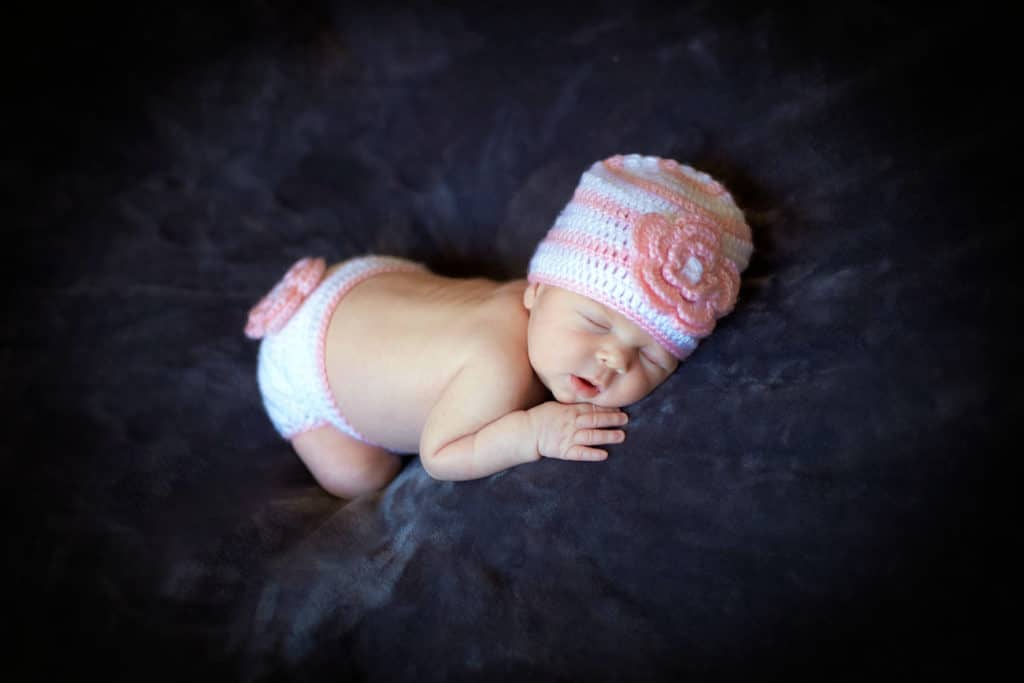 cozy sleeping newborn chin resting on hand big soft bean bag setting with pink wool accents at olive branch baby studio in mississippi by danielle jacqueline