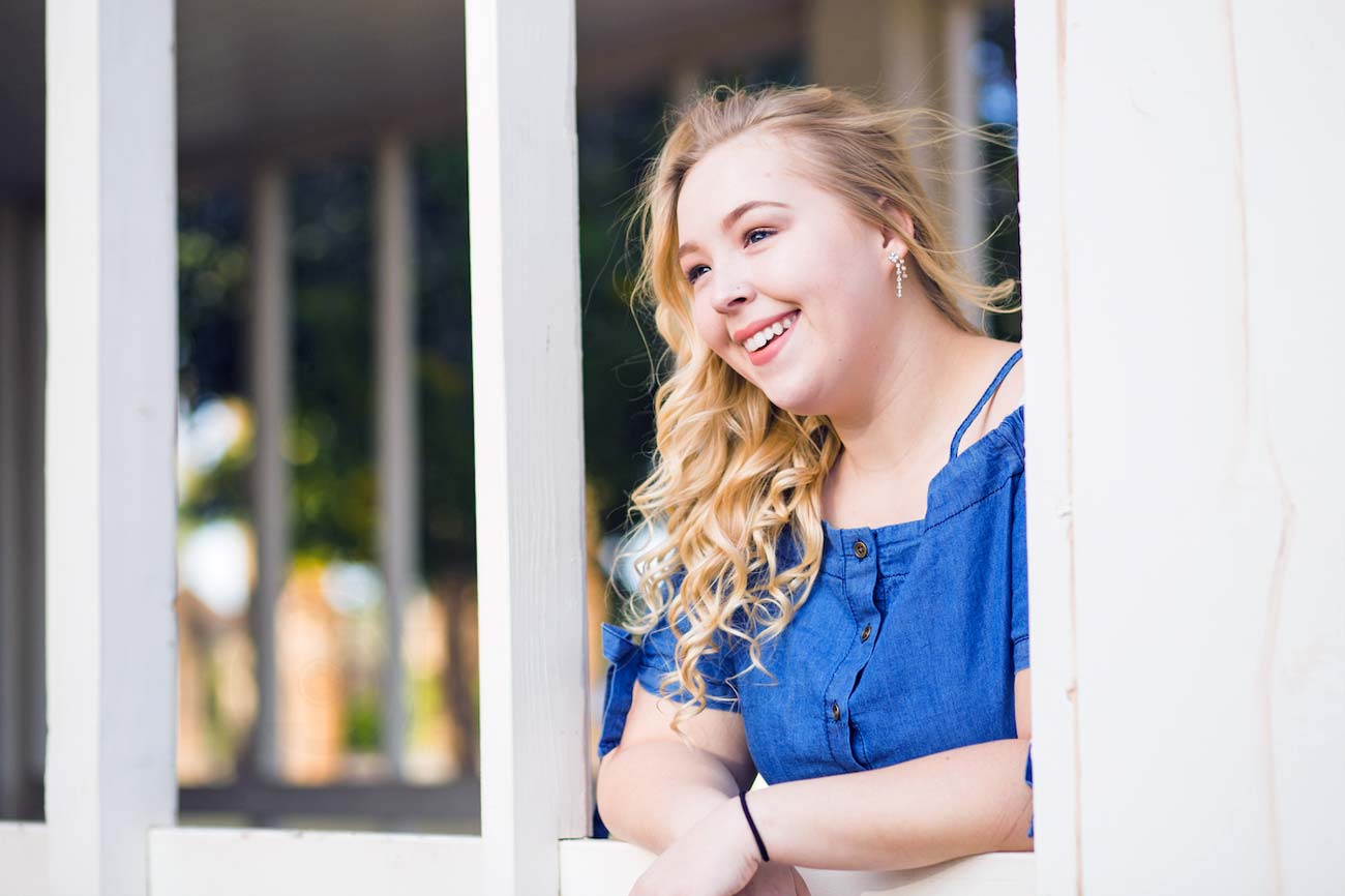 natural lighting and setting at local farm house on porch in collierville tn denim attire curled hair smiling off into the distance for up and coming actress and model captured by danielle jacqueline photography in olive branch