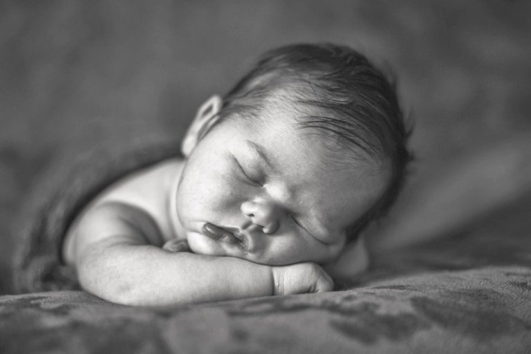 black and white close up photo of little boy arms folded under chin facing camera black and white soft resting place for newborn portraits at home for parents in desoto county ms