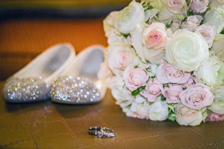 sparkling shoes of bride to be with couple's wedding rings and bouquet of pink and white flowers on wooden counter before wedding festivities begin in olive branch ms by danielle jacqueline photography