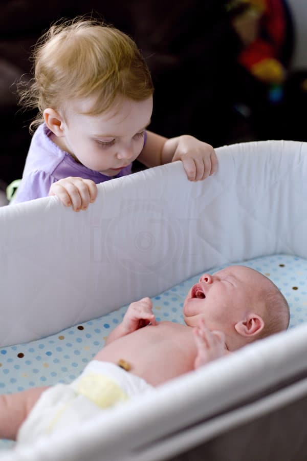 2 year old girl looking over crib of newborn baby brother crying she's concerned in love at hospital in memphis tennessee during photoshoot with danielle jacqueline photography adorable sessions