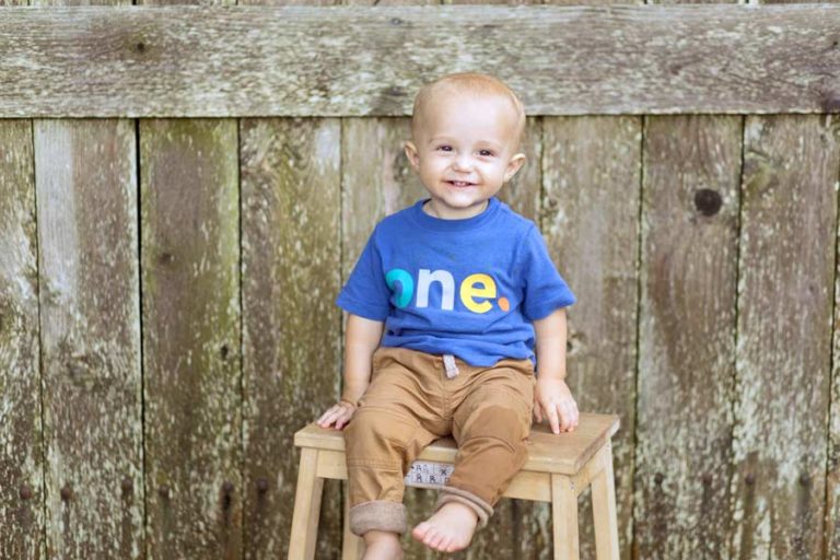 little one year old boy custom wooden backdrop for birthday photography session at danielle jacqueline outdoor venue in olive branch mississippi big smiles natural lighting discounts