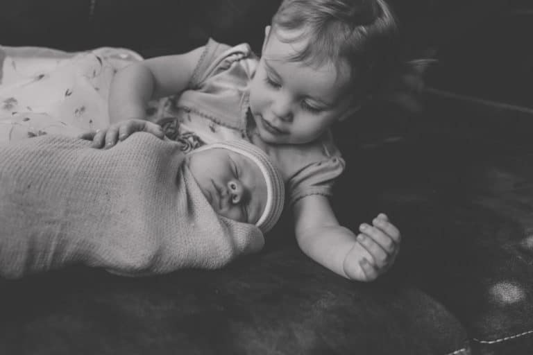 big sister laying with newborn baby brother on couch after mother gave birth to second child captured in black and white by danielle jacqueline photography in olive branch ms