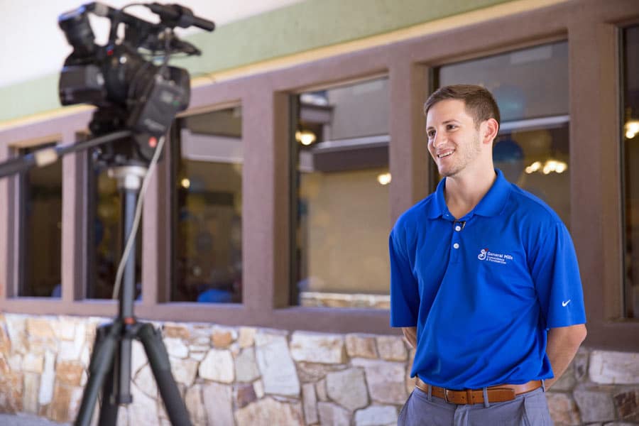 local reporter filming general mills pillsbury rep in blue shirt in pavilion with indoor photographer from memphis tennessee taking picture for public relations team