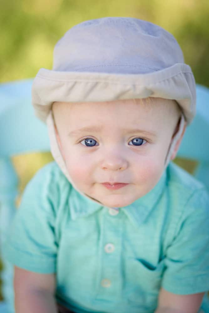 little blue eyed boy sailor hat green easter shirt looking up at camera on stool with mississippi grass in background for parents in memphis tn