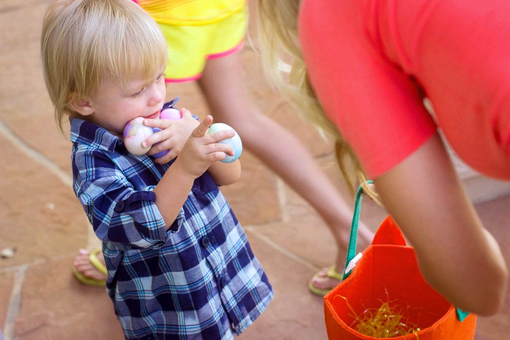 toddler on Easter trying to carry as many eggs as he can while looking to his mother for help in olive branch tn photographer