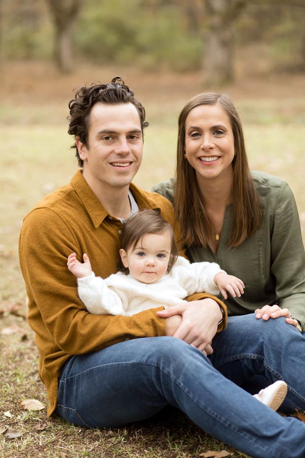 young couple with 1 year old daughter sitting on grass during fall extended family photoshoot at danielle jacqueline's outdoor venue in olive branch ms