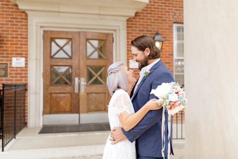 happily married couple standing in front of memphis tennessee wedding venue in each others arms dressed formally with ceremonial photographer and detailed planner north mississippi designs