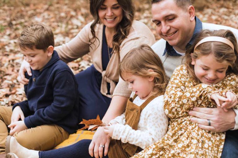 close up photography during extended family shoot of children being cuddled by father while playing in leaves with mommy looking and laughing on thanksgiving by danielle jacqueline in olive branch ms