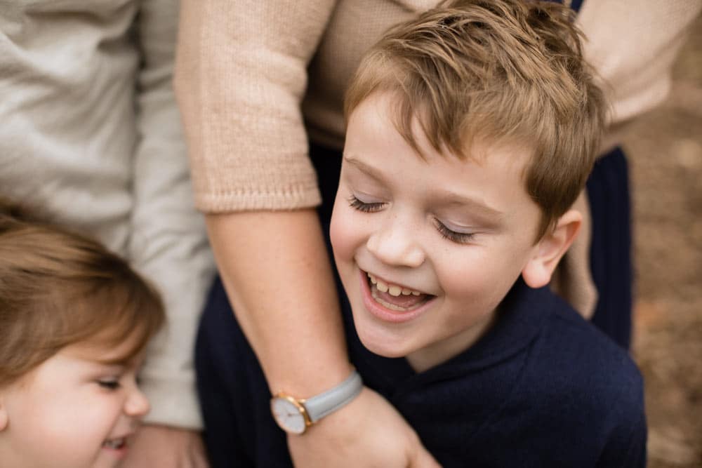 young boy laughing eyes close in mother's arms little sister in background during autumn photo shoot with danielle jacqueline for extended families on thanksgiving in olive branch ms