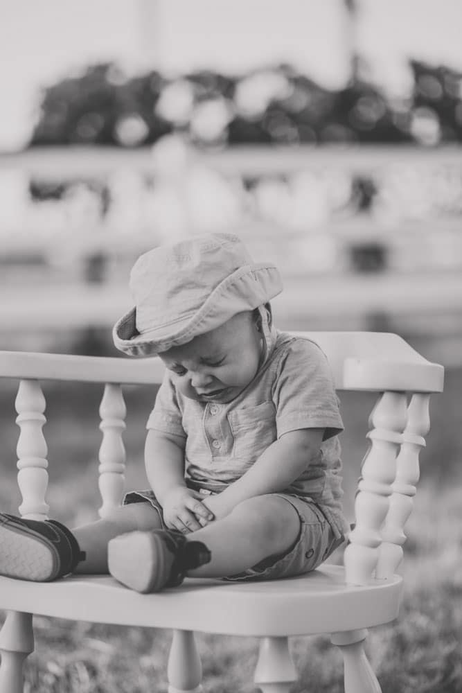 seated on bar stool baby boy cute hat white picket fence in background mississippi portrait sneezing eyes closed danielle jacqueline photography