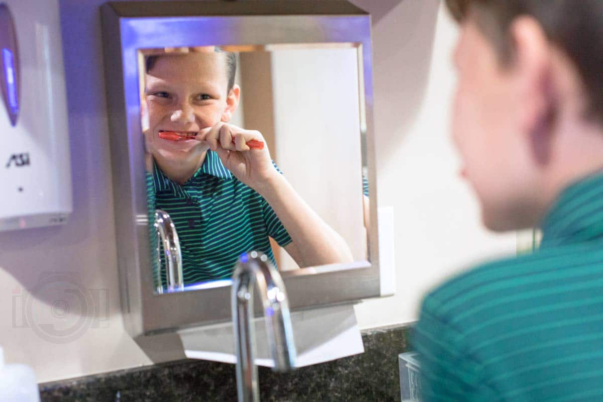 smiling young man at dental clinic brushing his teeth in mirror striped green and blue shirt for company website pictures by danielle jacqueline