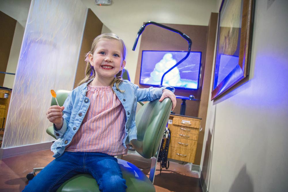 little girl in pigtails with sucker in hand smiling big for camera during local session with dental photographer now located in olive branch mississippi