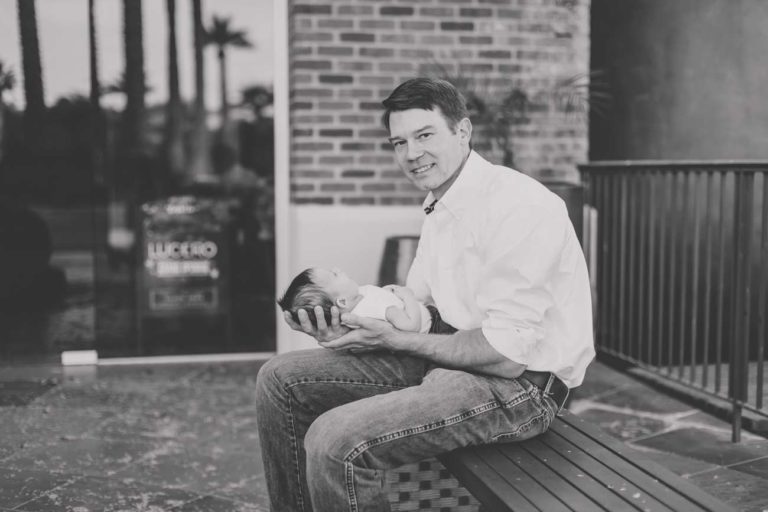 newborn baby boy in his daddy's arms outside the hospital on bench looking left at camera for black and white portrait in memphis tennessee by danielle jacqueline