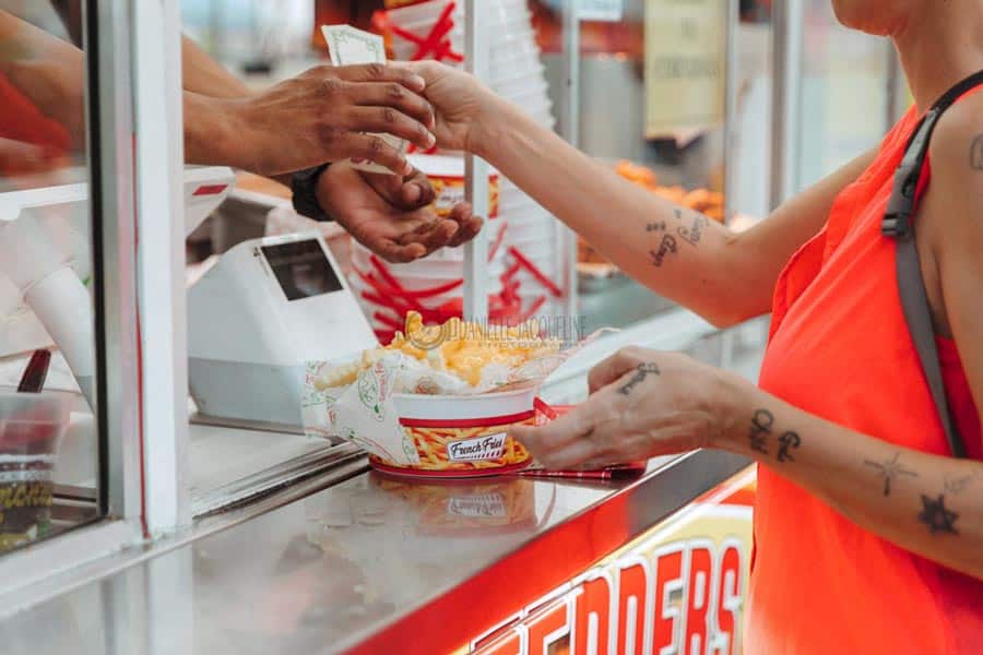 woman with tattoos on wrist and arms paying for and grabbing cheese fries and drink from food vendor truck photographer at midsouth fair in southaven mississippi september 2022