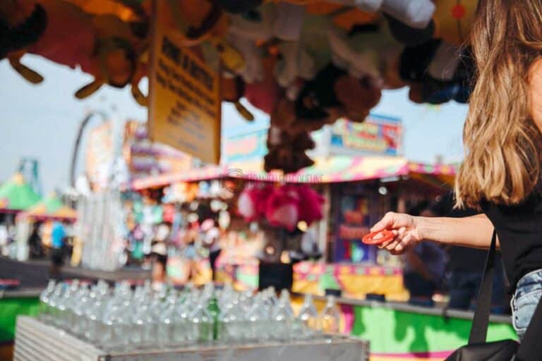 woman tossing red rind onto glass bottles carnival game with stuff animal prizes hanging from booth awning to win midsouth fair photography events memphis tn