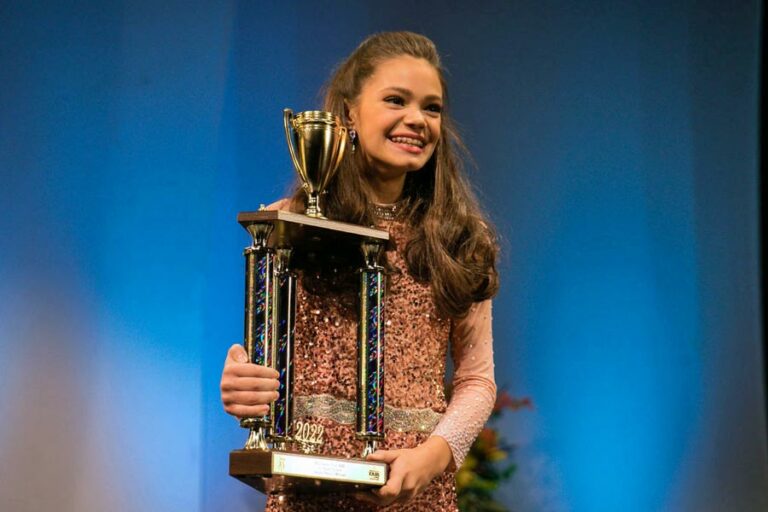 young girl holding huge trophy after winning talent show competition on stage at lander's center in southaven mississippi at midsouth fair 2022 by danielle jacqueline