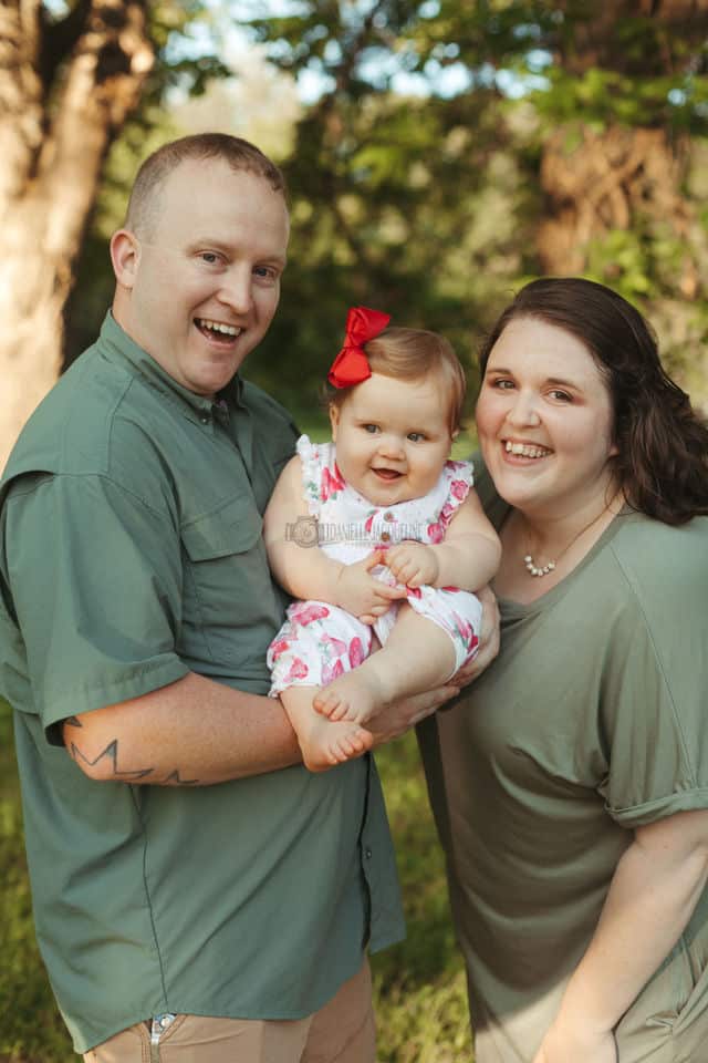 giddy father with daddies girl and mother of child looking at camera candid moment during family photo session outdoors mississippi professional portraits turning one parents