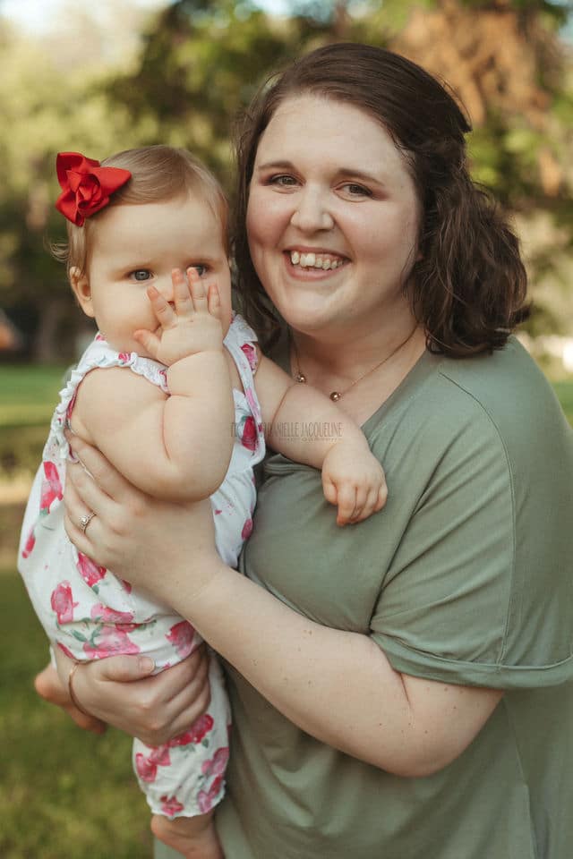 smiling mother with first born baby girl turning one hiring photographer packages smiling infant hand in face natural landscape venue olive branch mississippi