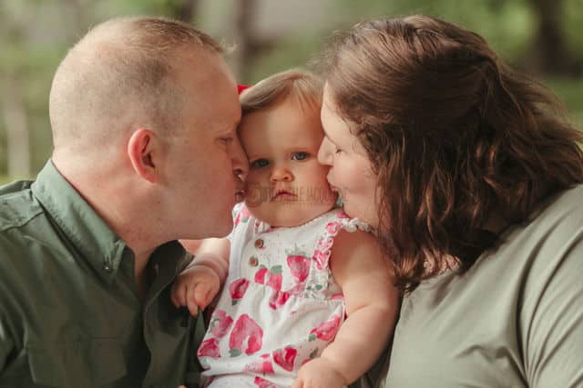 mom and daddy kissing one year old daughter on birthday for family cherished moments spring time by danielle jacqueline photography in desoto county