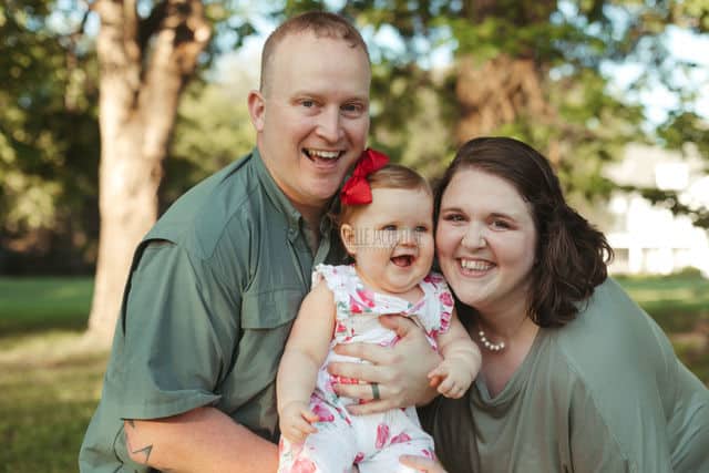 dad holding one year old daughter tightly while laughing during family photo session birthday celebration with danielle jacqueline photography in olive branch ms outdoors